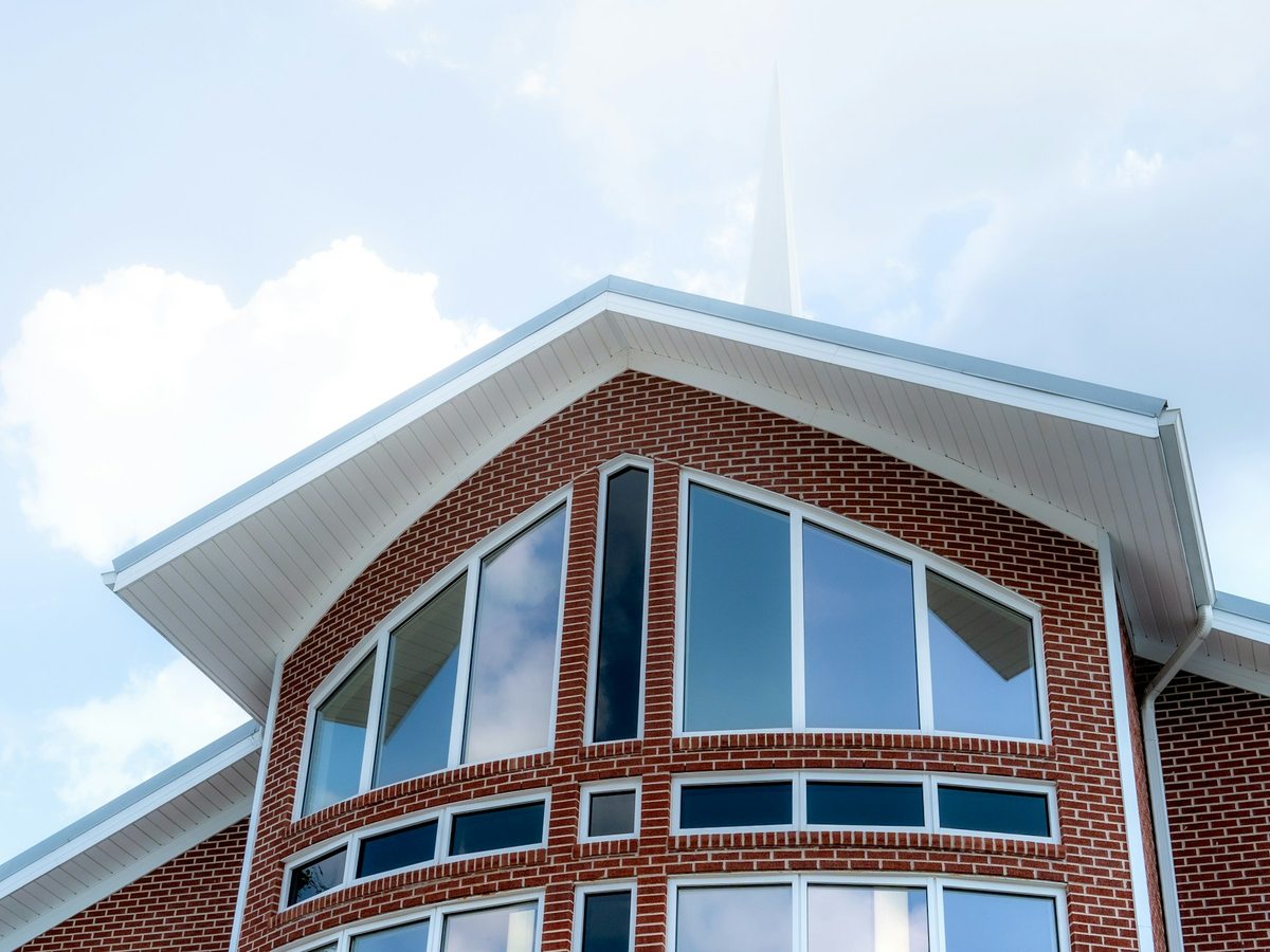Red-brick church facade with broad windows beneath a bright blue sky