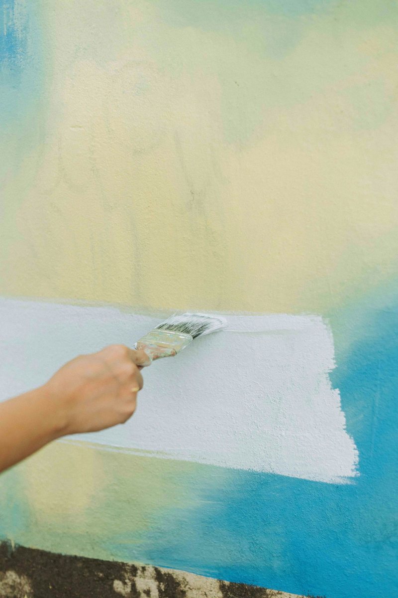 Illustrative trade photograph of a hand brushing fresh paint onto a colorful wall