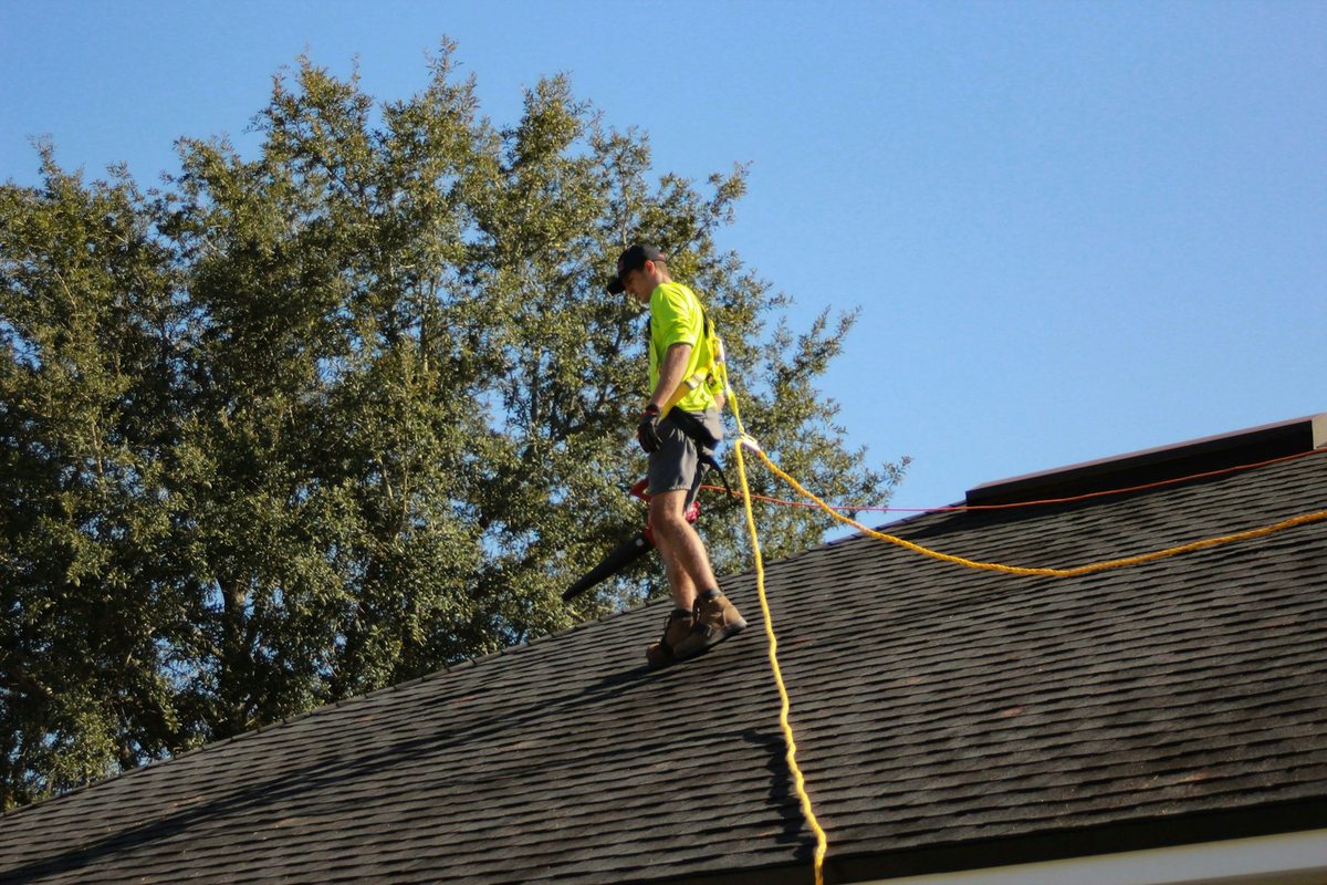 Illustrative trade photograph of a roofer working on an asphalt-shingle roof